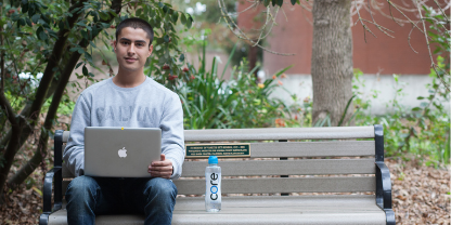 male student sitting on a bench using a laptop